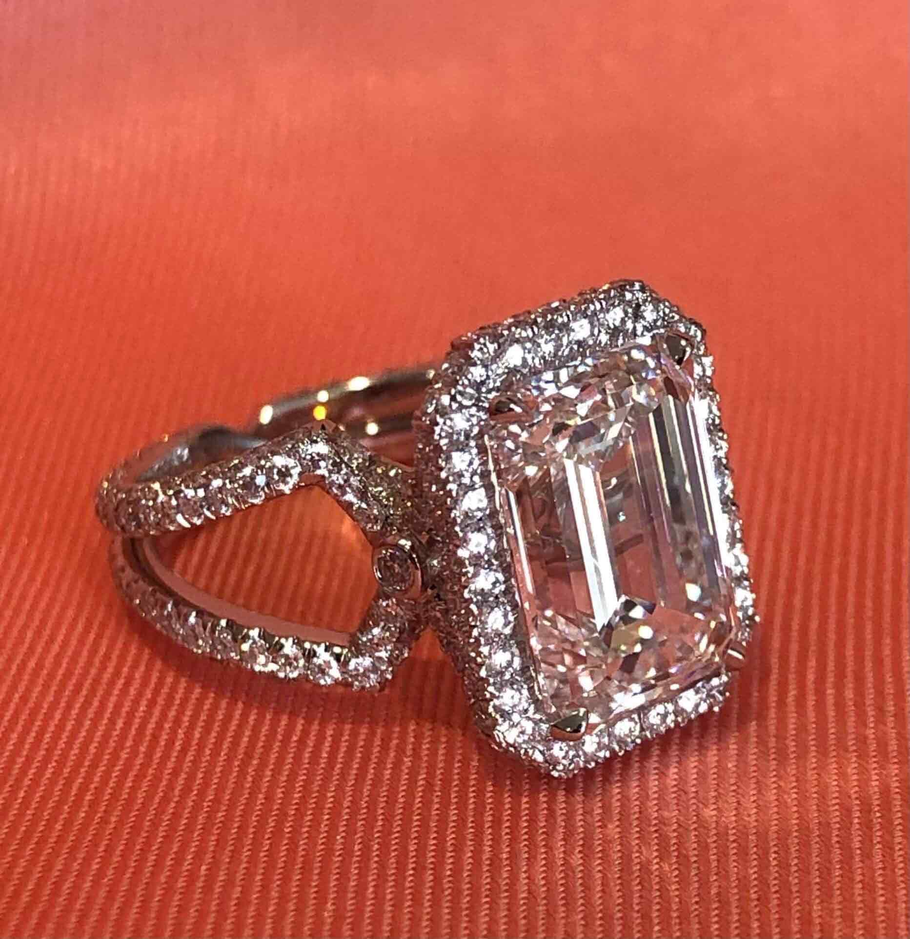 A tailor-made exquisite emerald-cut diamond ring featuring a radiant halo of 200 stones, ‘X’ on the side gallery, and an intricate band crafted with exceptional detail and elegance by Lindsey Scoggins.