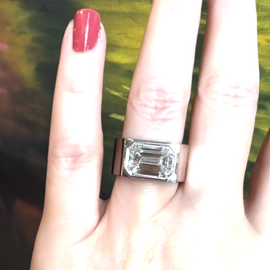 Close-up of a woman’s hand adorned with an emerald-cut white diamond platinum ring on her ring finger.