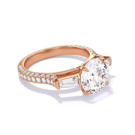 Rose gold engagement ring featuring a round diamond, baguette side stones, and a triple pavé diamond band.