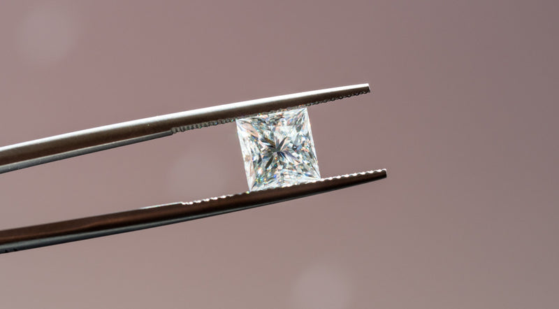 Close-up of a square-cut diamond held securely between metal tweezers.