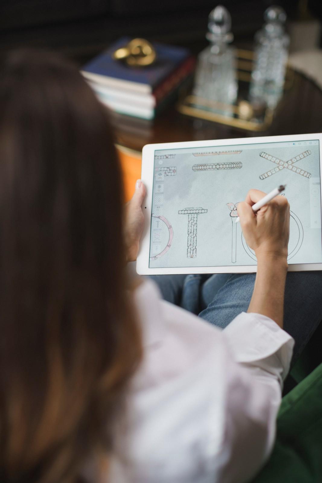 A woman sketching unique ring and jewelry designs on a tablet using a digital stylus.