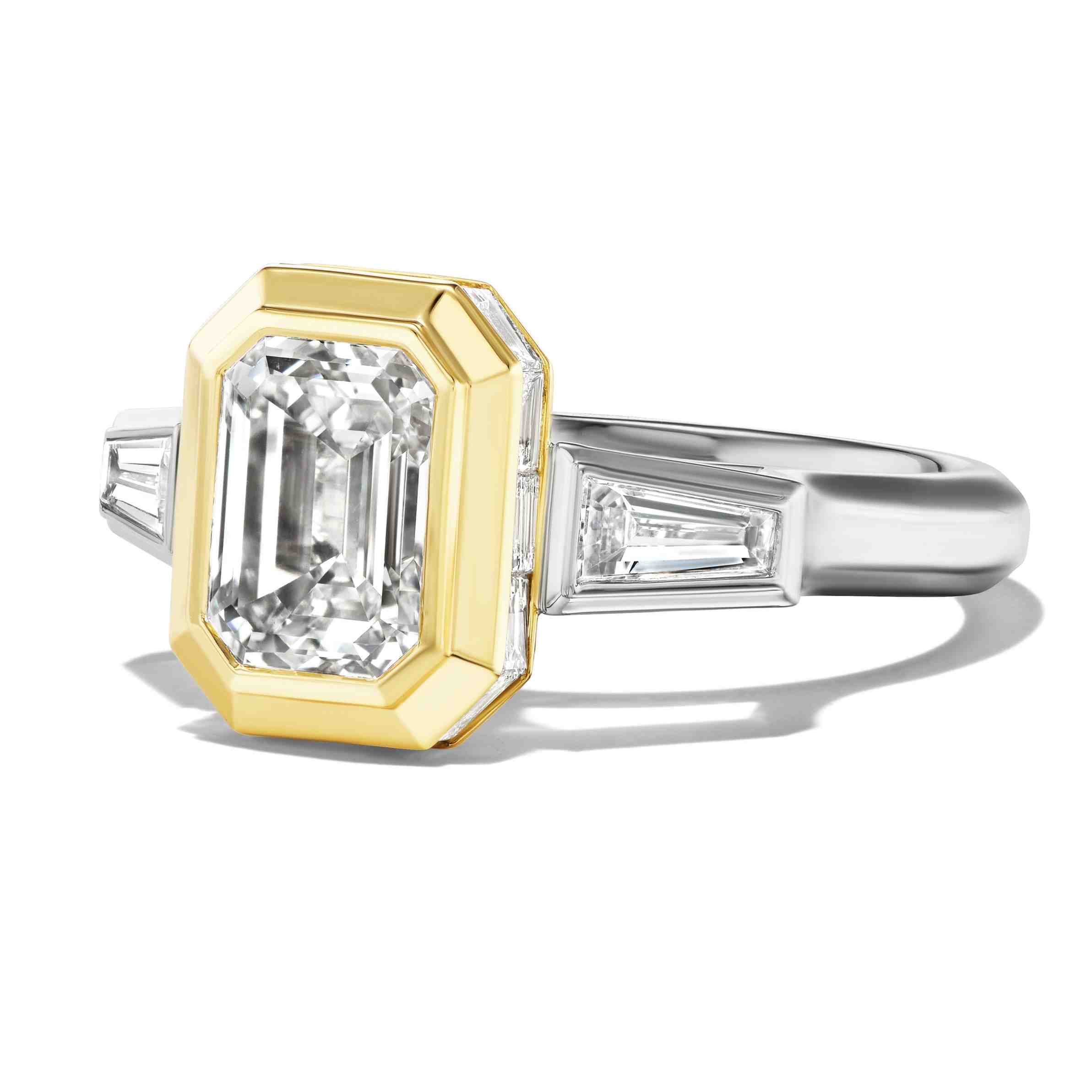 Emerald-cut diamond ring with a yellow gold bezel center and tapered side stones in white metal.