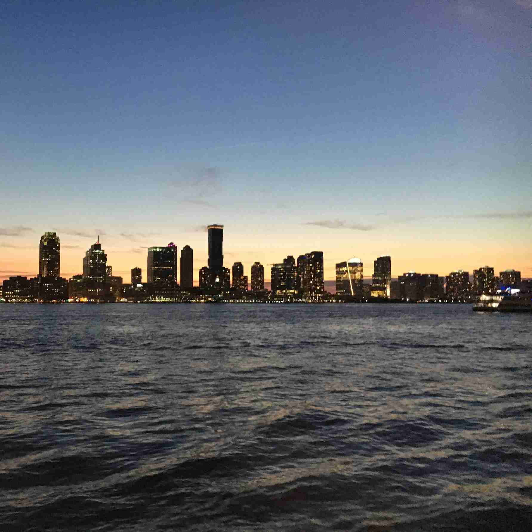 City skyline at sunset with lit buildings reflecting on the water and soft waves in the foreground.