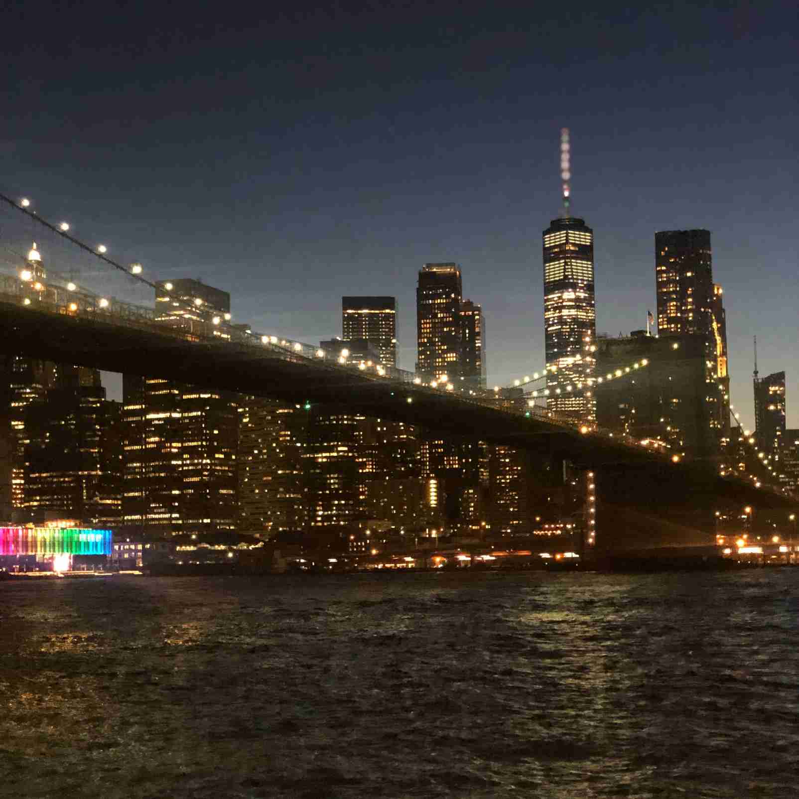 Brooklyn Bridge and New York skyline glowing at night with shimmering reflections on the water.
