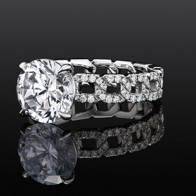 Close-up of a platinum chain-link ring with a round diamond center and pavé diamonds, shown on a glossy black surface.