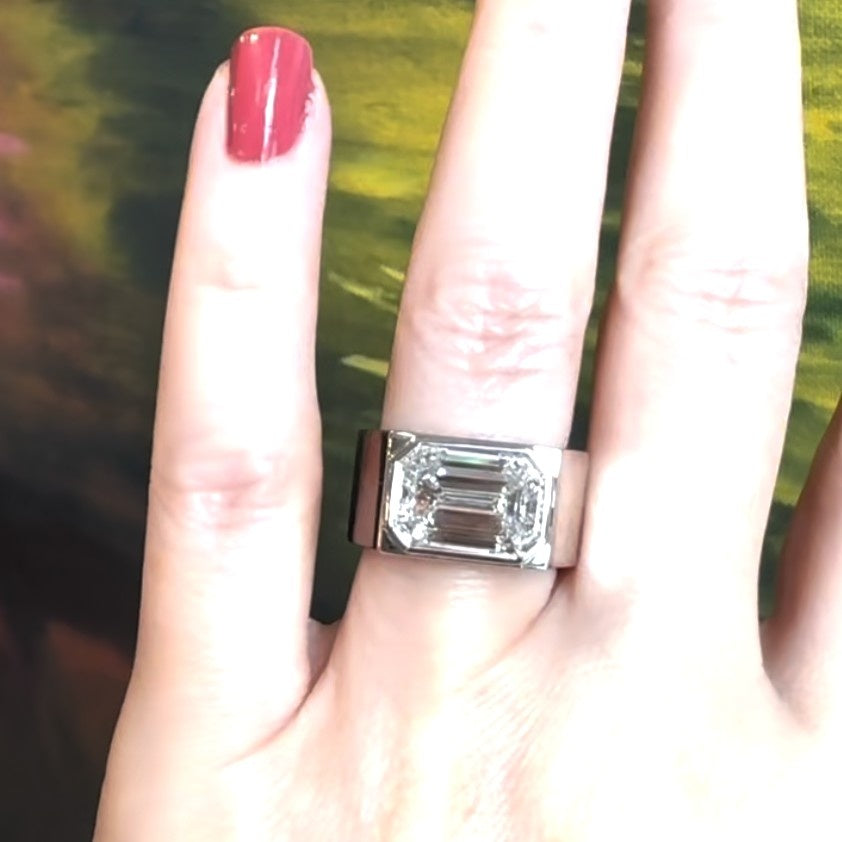 Close-up of a woman’s hand adorned with an emerald-cut white diamond platinum ring on her ring finger.