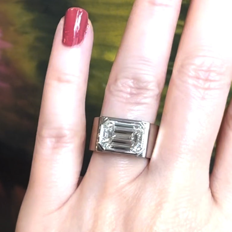 Close-up of a woman’s hand adorned with an emerald-cut white diamond platinum ring on her ring finger.
