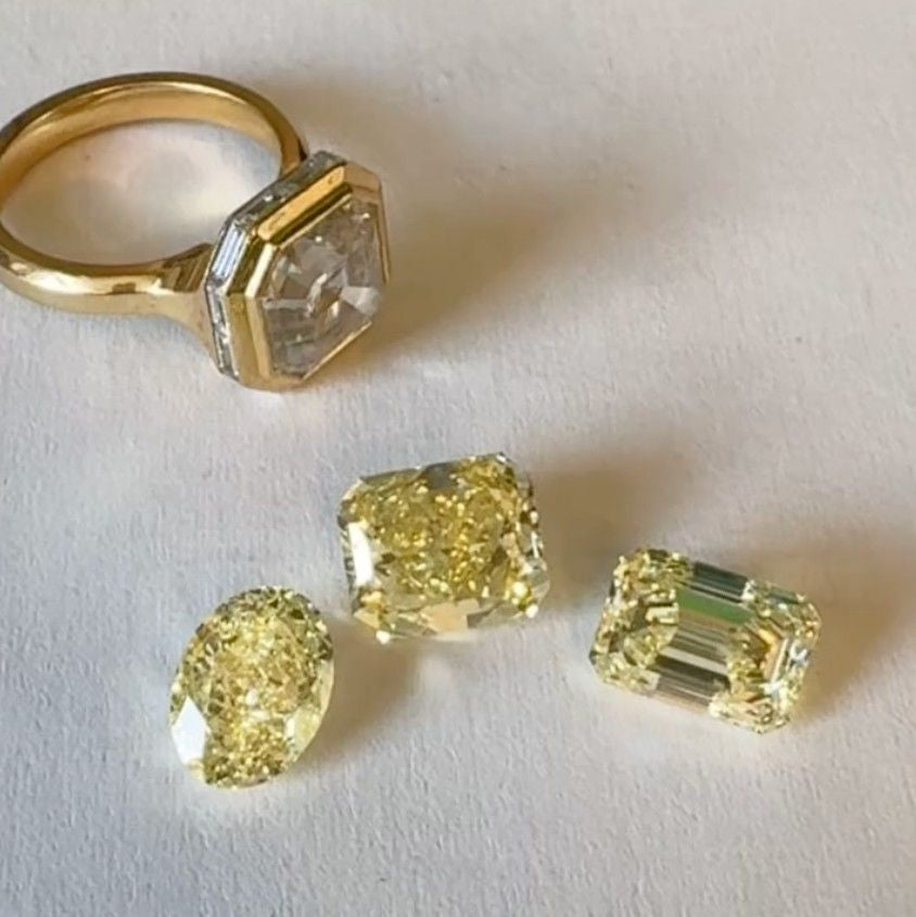 Gold ring with a clear asscher-cut diamond shown next to three loose yellow diamonds in oval, radiant, & emerald cuts.