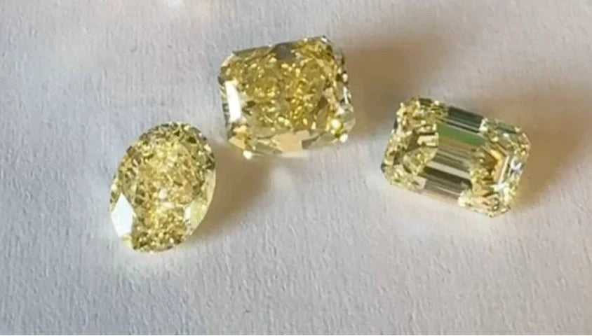 Collection of yellow diamonds in oval, Asscher-cut, and emerald-cut shapes displayed against a white background.