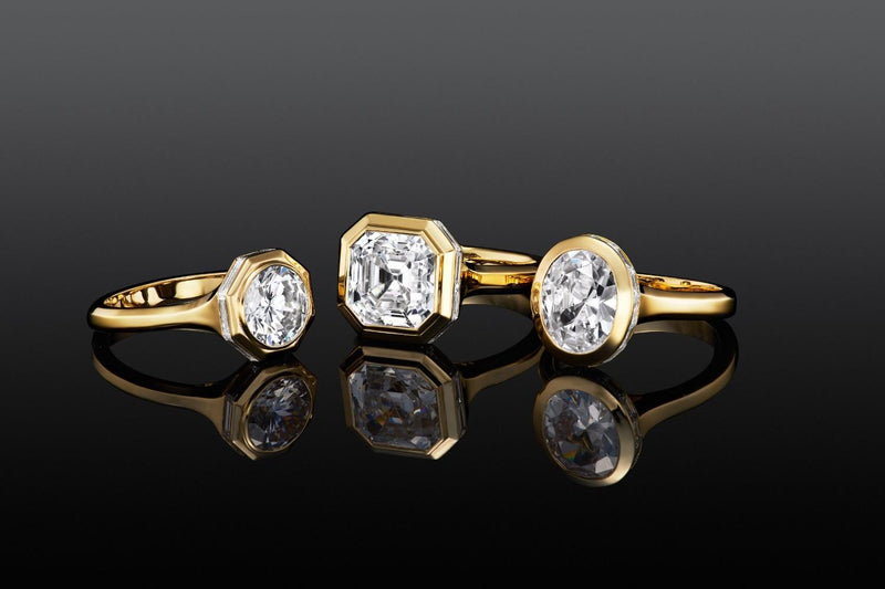 Three yellow gold bezel-set diamond rings featuring round, square, and oval center stones on a black background.