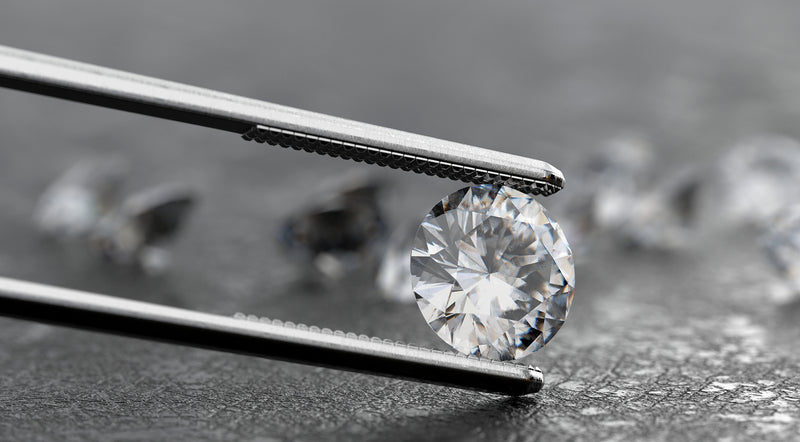 Close-up view of a white diamond securely held by white tweezers against a neutral background.