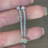 A hand holding a pair of long diamond tennis-style drop earrings by Lindsey Scoggins Studio.