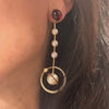 A person wearing a drop earring with a garnet stud, pearls, and a planetary hoop.