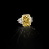Radiant-cut yellow diamond ring with white trapezoid side stones displayed against a black background.