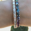 A wrist wearing a diamond emerald-cut tennis bracelet and a multi-colored gemstone bracelet by Lindsey Scoggins Studio.