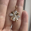 A hand holding a rose gold clover pendant with pear-shaped diamonds.