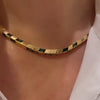 A person wearing a thick gold collar necklace with square blue tourmalines.