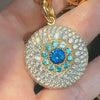 Close-up of a gold evil-eye pendant with blue center stones and a halo of white diamonds.