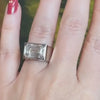 Close-up of a woman’s hand adorned with an emerald-cut white diamond platinum ring on her ring finger.