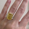 Close-up of a woman's hand wearing an emerald-cut yellow diamond ring with two white baguette side stones.