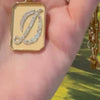 Woman’s hand holding a rectangular gold locket featuring a “D” initial pendant inside.