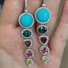 A hand holding a Custom Turquoise, Gemstone, and Diamond Earrings with Sleeping Beauty turquoise and indicolite tourmaline.