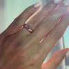 A hand wearing an 18k rose gold wedding band with a pink sapphire heart.