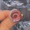 A hand holding a pink tourmaline ring with a diamond crescent moon setting.