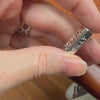 A hand holding a sterling silver Emotion Necklace with names of various emotions engraved.