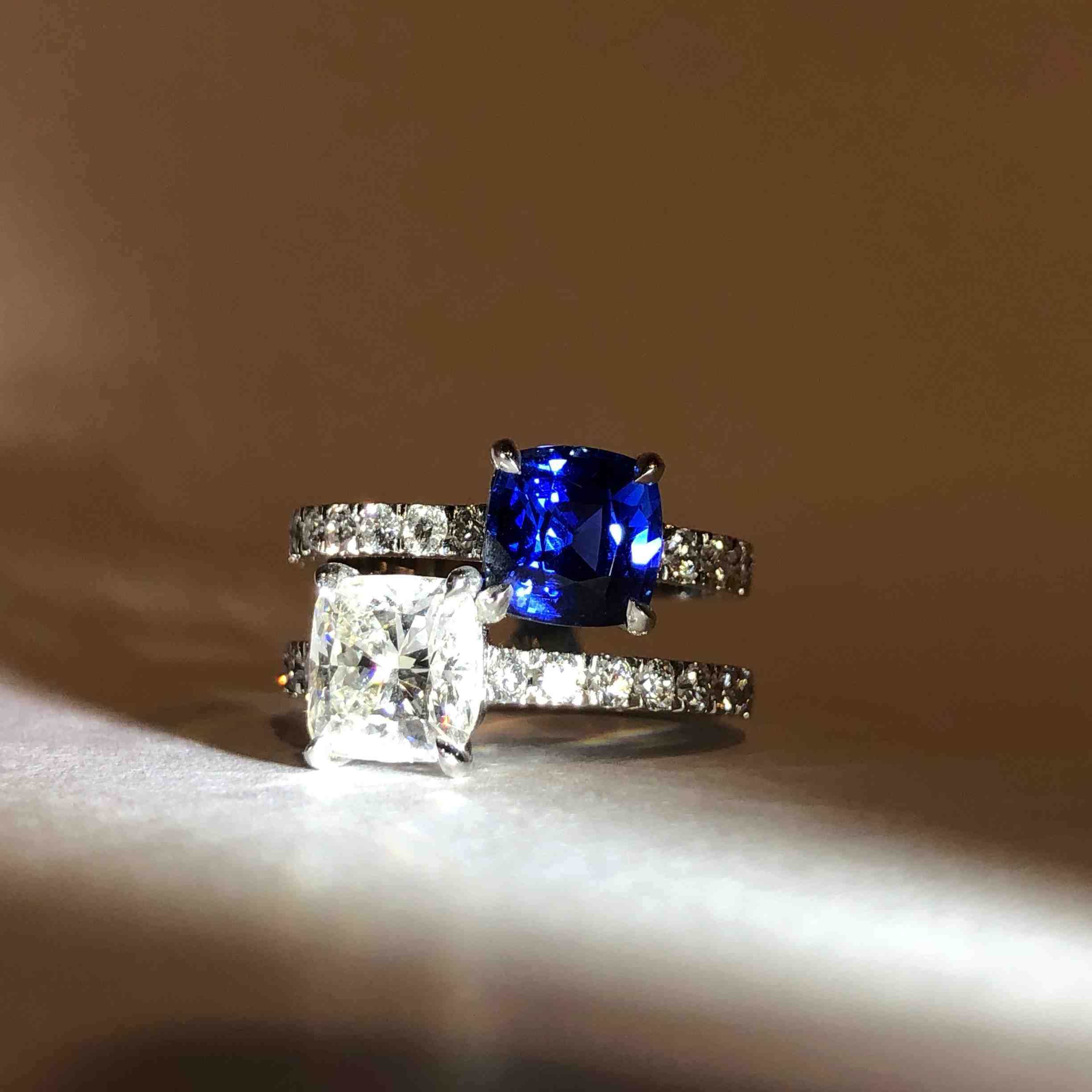 Close-up of a two-stone ring featuring a blue sapphire and a white diamond on a pavé band.